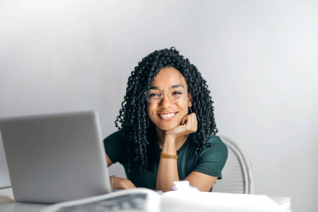 Black woman at a laptop, looking up and smiling at camera