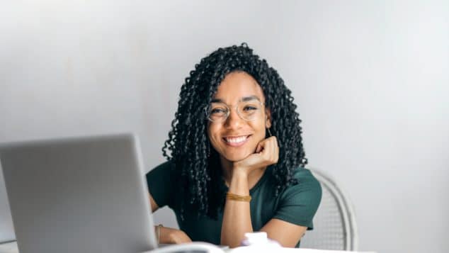 Black woman at a laptop, looking up and smiling at camera