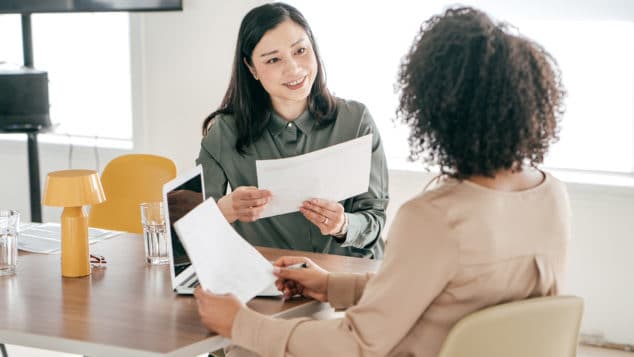 An interviewer looks over documents while speaking with a potential candidate.