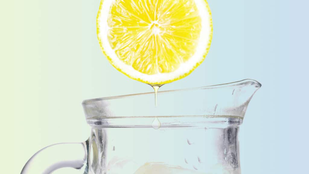 A lemon gets squeezed into a pitcher of lemonade.