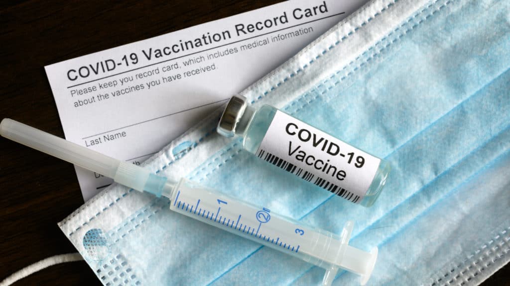 A mask and needle and vial with the covid vaccine, and vaccine card