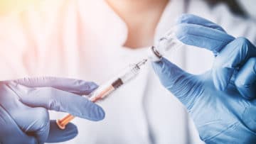 Close up of a nurse in gloves drawing a vaccine into a syringe