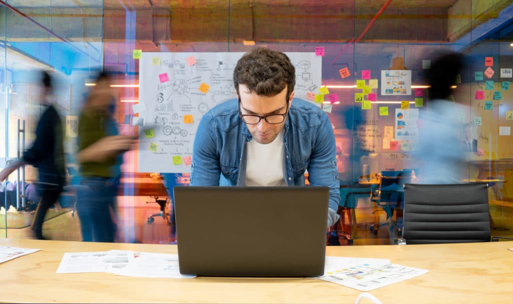 Marketing pro working at a creative office using his computer and people moving at the background - place of work concepts