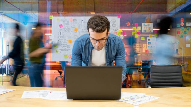 Marketing pro working at a creative office using his computer and people moving at the background - place of work concepts