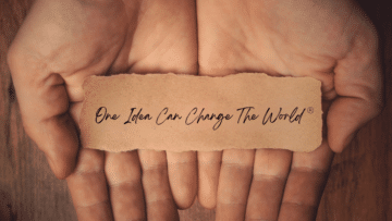 Hands holding a small brown slip of paper that reads "One Idea Can Change the World"