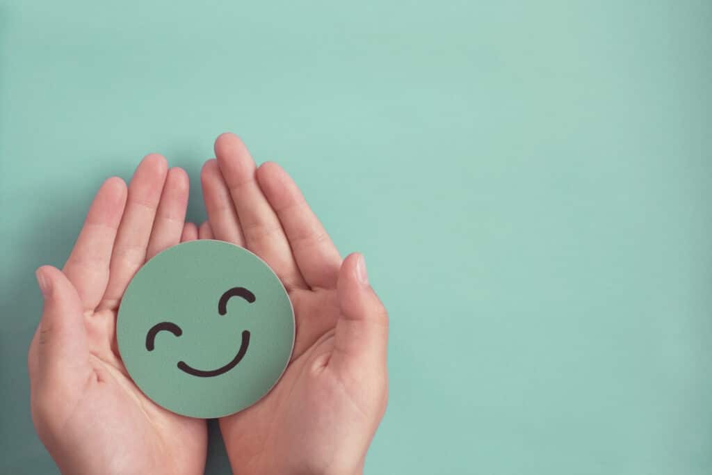 Hands holding green happy smile face paper cut, good feedback rating and positive customer review, experience, satisfaction survey ,mental health assessment, child wellness,world mental health day concept